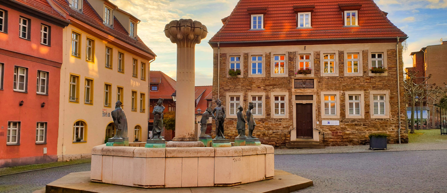 St. Katharinenstift und Knappenbrunnen - Ein Steinmauergebäude und ein Brunnen mit Figuren des Berg- und Hüttenwesens im Vordergrund.