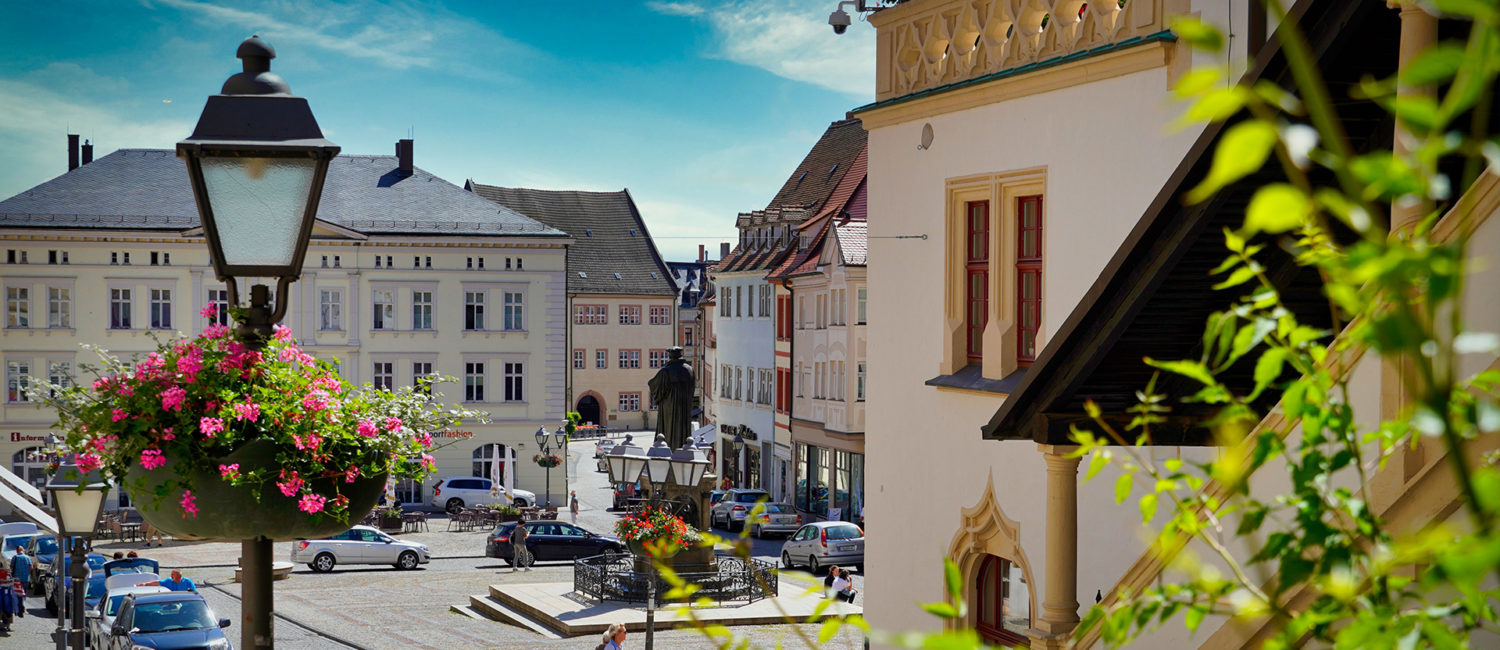 Markt und Lutherdenkmal mit grünen Zweigen und Laterne mit Blumenampel im Vordergrund