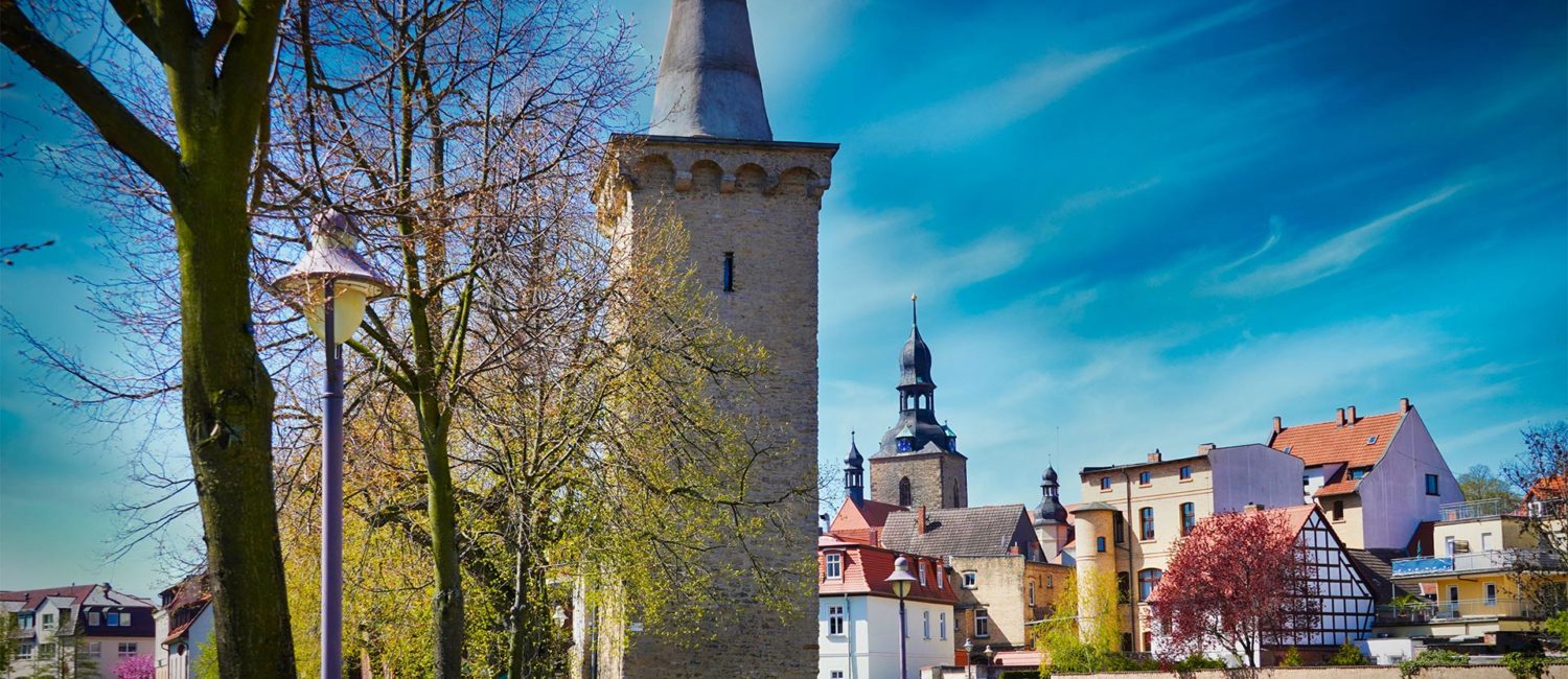 Hettstedt - Stadtmauer Turm "Kunstzuckerhut" neben der Wipper und blühenden Bäumen mit Gebäuden im Hintergrund